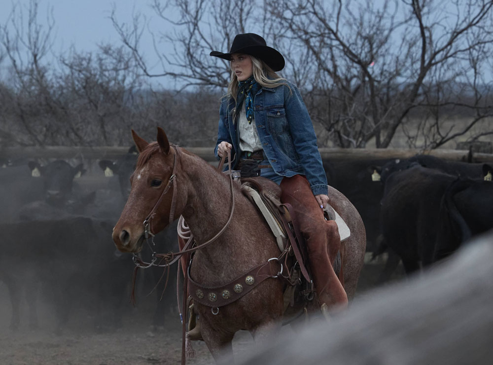 A woman wearing a black cowboy hat while riding a horse 